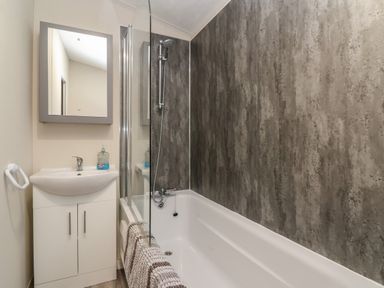 A bathroom with a bathtub shower combination a white sink with cabinet and a rectangular mirror at Longdon Lodge in Wickhamford near Evesham