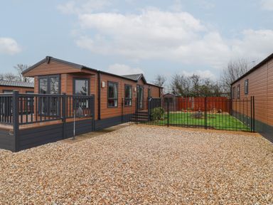 A wooden mobile home with a black railing deck and a fenced garden with green lawn