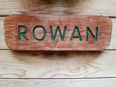 A wooden sign with the word Rowan engraved on it placed on a wooden surface at Rowan Lodge in Rosliston