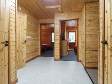 A corridor with wooden walls and ceiling leading to bedrooms with red bedding at Rowan Lodge in Rosliston