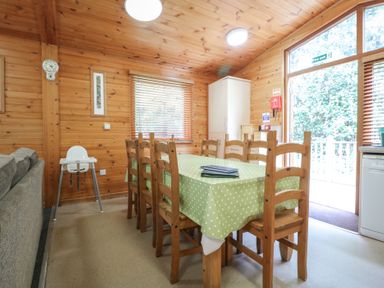 A dining area with wooden chairs around a table with a green polka dot tablecloth and a high chair by the window at Oak Lodge in Rosliston