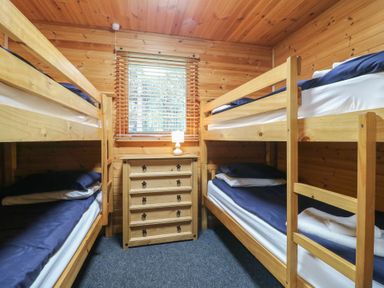 A bedroom with two wooden bunk beds a chest of drawers a lamp and a window at Oak Lodge in Rosliston