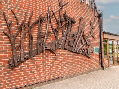 A brick wall with large wooden art resembling tree branches and leaves at Oak Lodge in Rosliston