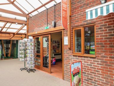 An entrance to a shop with glass doors a display stand with postcards a brick wall with a window and an ice cream advertisement at Oak Lodge in Rosliston