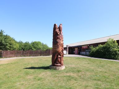 A carved wooden sculpture on grass near a visitor centre building with trees and a wooden fence at Oak Lodge in Rosliston