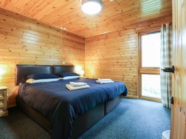 A bedroom with a double bed towels on bed wooden walls window with curtains at Chestnut Lodge in Rosliston