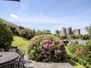 A garden with flowering bush and patio furniture overlooking a castle at Bryn Awelon in Harlech