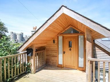 A wooden porch with a front door and railing with a castle in the background at Bryn Awelon in Harlech