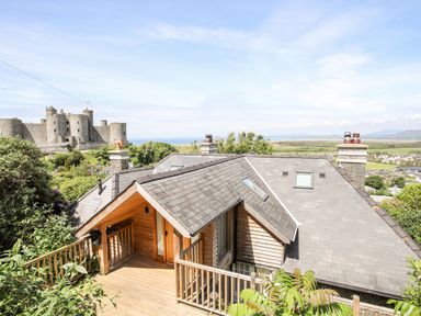 A house with a wooden deck and slate roof near a large stone castle and countryside at Bryn Awelon in Harlech