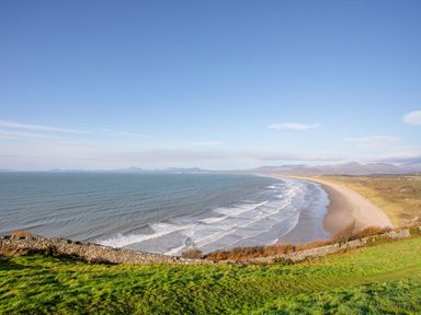 A coastline with waves along a sandy beach and grassy foreground at Bryn Awelon in Harlech
