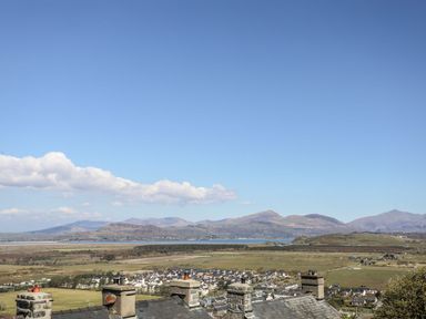 A landscape view of rooftops a town fields and distant mountains under a blue sky at Bryn Awelon in Harlech