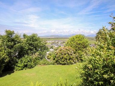 A garden with lush green grass and shrubs overlooking a town and distant mountains at Bryn Awelon in Harlech