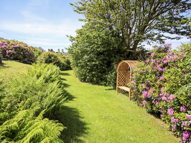 A garden pathway with green grass a wooden bench and green and purple flowering bushes at Bryn Awelon in Harlech