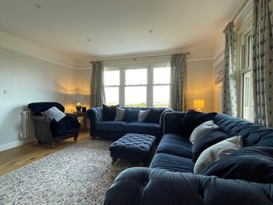 A living room with blue sofas armchair ottoman and curtains at Bryn Awelon in Harlech