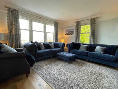 A living room with two blue sofas a matching ottoman a patterned rug and large windows at Bryn Awelon in Harlech