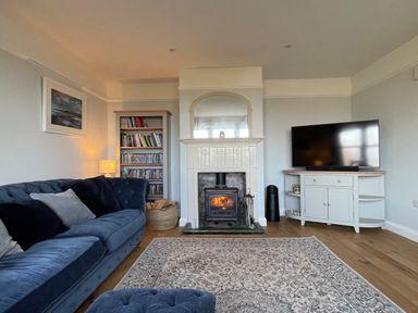 A living room with a blue sofa a wood burning stove bookshelves and a television at Bryn Awelon in Harlech