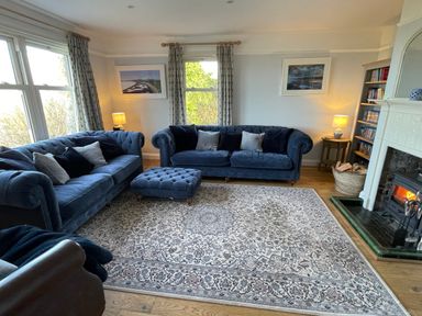 A living room with blue sofas a patterned rug a fireplace and bookshelves at Bryn Awelon in Harlech