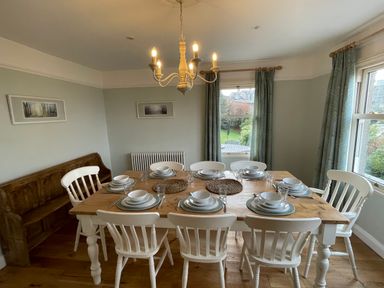 A dining room with a wooden table set for eight and white chairs at Bryn Awelon in Harlech
