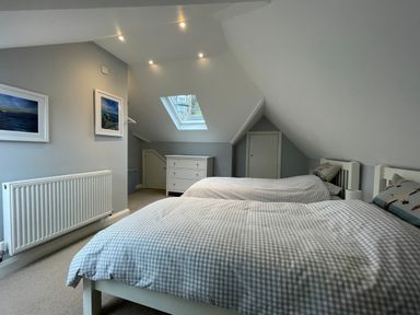 A bedroom with two single beds a chest of drawers skylight and framed pictures at Bryn Awelon in Harlech