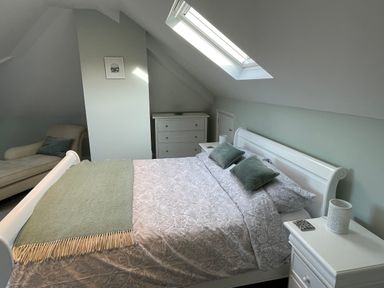 A bedroom with a bed, pillows, a blanket, a bedside table, a chair, and a chest of drawers at Bryn Awelon in Harlech