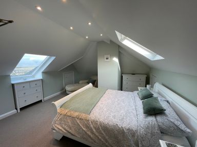 A bedroom with a double bed two dressers a chaise lounge and skylight windows at Bryn Awelon in Harlech