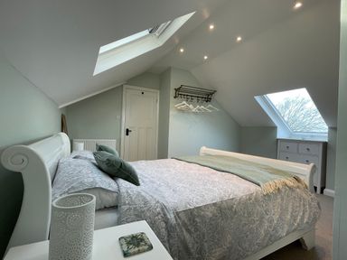 A bedroom with a bed side table a bed two skylight windows a chest of drawers and a wall mounted coat rack with hangers at Bryn Awelon Harlech