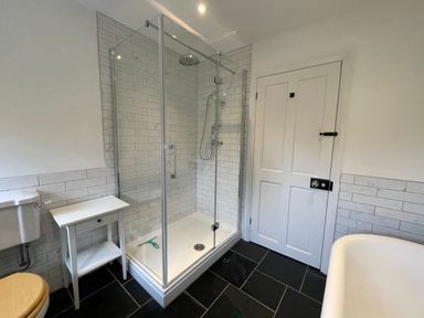 A bathroom with a glass shower enclosure a white wooden table a white door and a bathtub at Bryn Awelon in Harlech