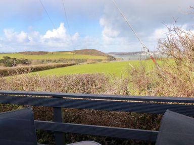A balcony with two chairs overlooking green fields hills and a body of water at Little Trevorrick Caravan in St Issey