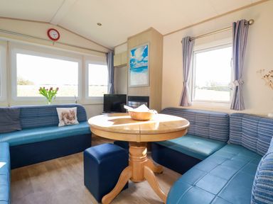 A dining area with a round wooden table surrounded by blue cushioned seating and a small TV at Little Trevorrick Caravan in St Issey