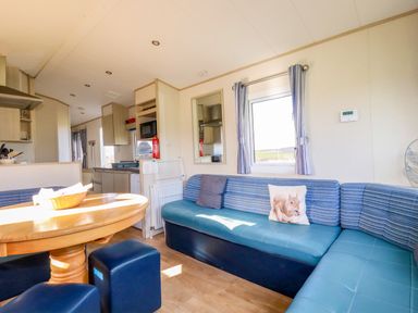 A living area with a wooden table surrounded by navy blue seats and a blue L-shaped sofa with cushions at Little Trevorrick Caravan in St Issey