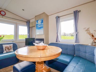 A dining area with a round wooden table and blue cushioned seating around it at Little Trevorrick Caravan in St Issey