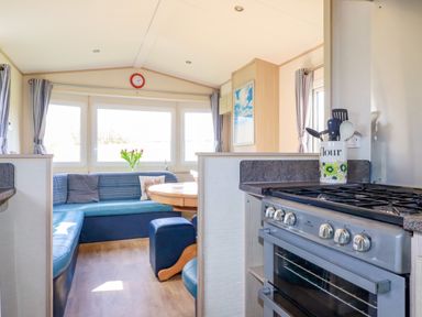 A kitchen with a stove and cooking utensils next to a dining area with a round table and bench seating at Little Trevorrick Caravan in St Issey