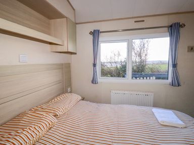 A bedroom with a bed with striped bedding and a window with curtains at Little Trevorrick Caravan in St Issey