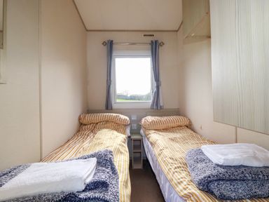 A small bedroom with two single beds and a window between at Little Trevorrick Caravan in St Issey