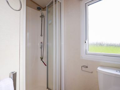A shower with sliding glass doors next to a window and a toilet with an empty toilet paper holder at Little Trevorrick Caravan in St Issey