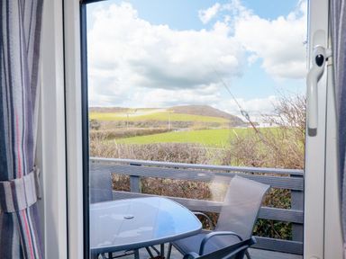 An outdoor patio with chairs and a table overlooking green fields and hills at Little Trevorrick Caravan in St Issey