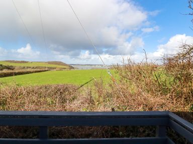 A view of green fields bushes and a body of water under a partly cloudy sky at Little Trevorrick Caravan in St Issey