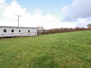 A grassy field with a caravan and wooden fence under a partly cloudy sky at Little Trevorrick Caravan in St Issey