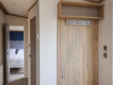 A hallway with wooden coat hooks and a view of a bedroom with a bed at Maple Lodge in Whitby