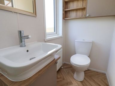 A bathroom with a white sink and faucet a toilet a window and wooden shelves at Maple Lodge in Whitby