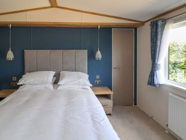 A bedroom with a bed a headboard two bedside tables hanging lamps a door and a window with curtains at Maple Lodge in Whitby