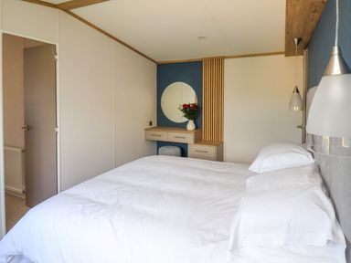 A bedroom with a bed white bedding a dressing table with a round mirror and flowers at Maple Lodge in Whitby