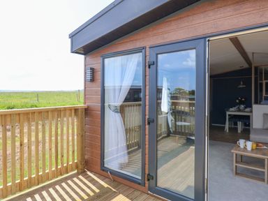A wooden deck with a railing outside a room with glass doors and curtains at Maple Lodge in Whitby