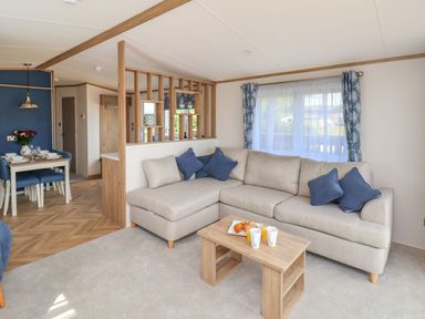 A living room with a beige sectional sofa with blue cushions and a wooden coffee table with cups and croissants at Fir Lodge in Whitby