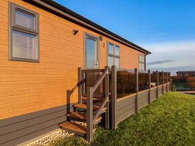 An exterior view of a wooden building with steps leading to a door and a railing on a grassy area at Cherry Blossom Lodge in Whitby
