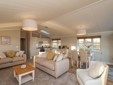 A living room with two beige sofas a coffee table an armchair and an open kitchen with a dining table and chairs at Cherry Blossom Lodge in Whitby