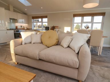A beige sofa with cushions in an open-plan room with a kitchen and dining area at Cherry Blossom Lodge in Whitby