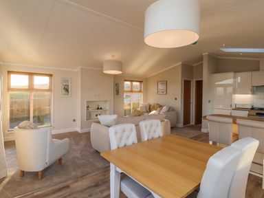 An open plan living and dining room with beige armchairs dining table and kitchen at Cherry Blossom Lodge Whitby