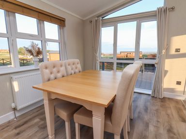 A dining area with a wooden table and four upholstered chairs near windows and glass doors at Cherry Blossom Lodge in Whitby