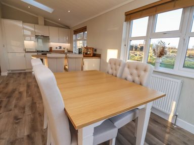 A dining table with upholstered chairs and a kitchen area with cabinets and bar stools near a window at Cherry Blossom Lodge in Whitby